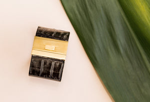 Wide Turnlock Black Dyed Croc Cuff on pink background with green leaf